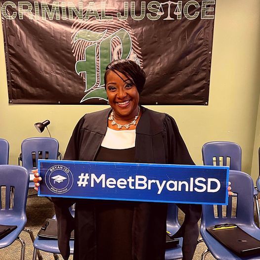 Phe'Licia 'Mrs. T' Thompson smiling & holding a blue #MeetBryanISD sign