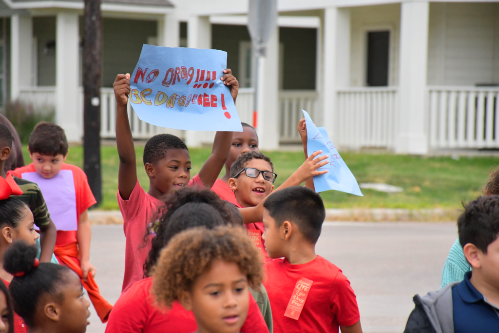 Crockett Elementary students walking in the Red Ribbon Parade and holding signs that read "No Drug!!!! Be Drug Free!"