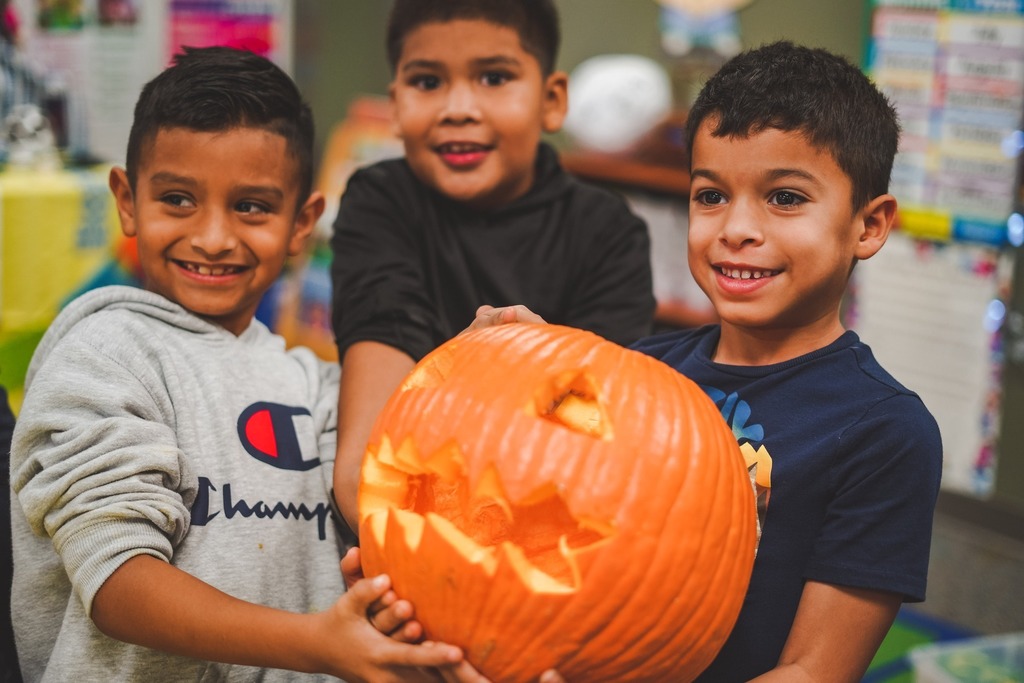 Three boys smiling while holding a pumpkin